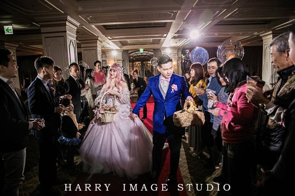 這張照片是一對新人正在舉行婚禮,新郎穿著藍色西裝,新娘穿著粉紅色的婚紗,他們正準備交換戒指,周圍的賓客都為他們歡呼。