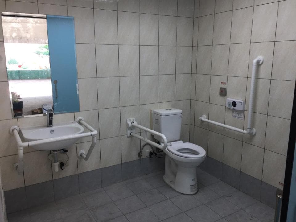 這張照片是一個無障礙的洗手間,有扶手和適合輪椅使用的馬桶。