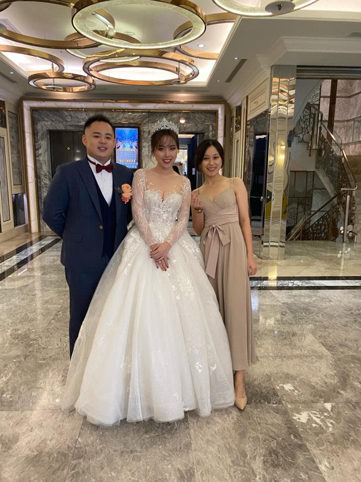 這張「婚禮」的照片是一對新人和一位女伴站在飯店大廳。 新娘穿著白色婚紗,新郎穿著深藍色西裝,女伴穿著米白色禮服。