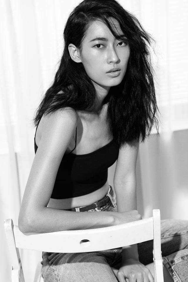 這張「年輕女性」的照片是一個穿著黑色背心和牛仔褲的女生坐在白色的椅子上,她有一頭長髮和憂鬱的表情。