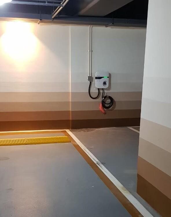 這張照片是一個充電站,牆壁上有一個白色的充電器,上面有一個綠色的指示燈,旁邊有電線。