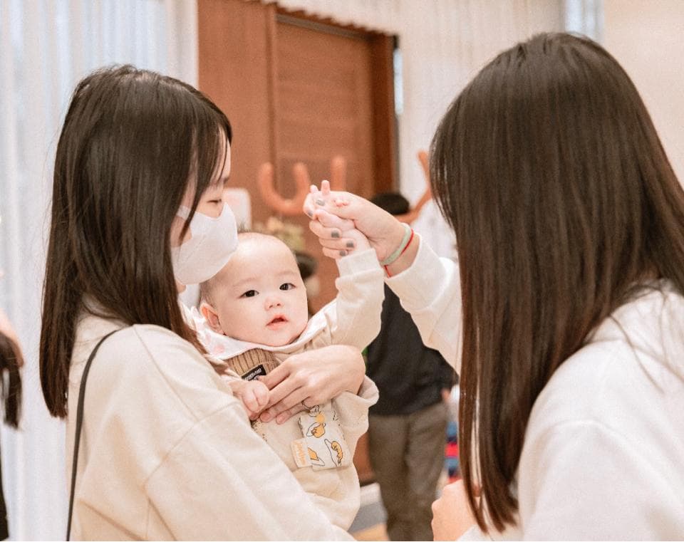 這張「一位媽媽抱著嬰兒,另一位女性站在她們旁邊」的照片是。媽媽戴著口罩,嬰兒微笑看著鏡頭,站在旁邊的女性似乎要伸手去觸碰嬰兒。