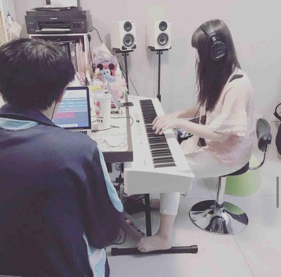這張「一位女生彈奏電子琴」的照片是一個女生坐在椅子上彈奏白色電子琴,而另外一個人則坐在她旁邊。