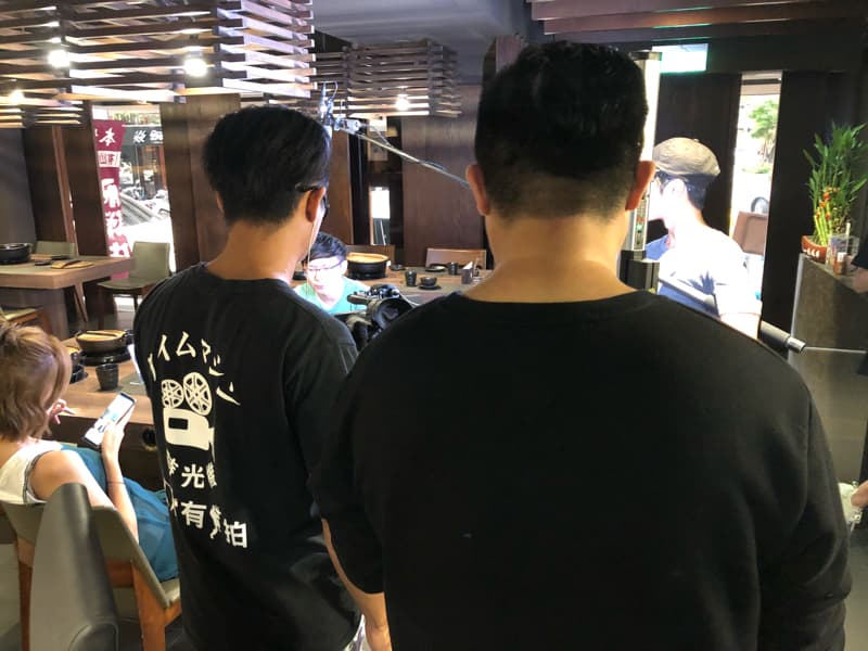 這張「拍攝」的照片是三個人在餐廳裡,其中兩個人站在一起,一個人坐在椅子上,他們好像正在拍攝節目。